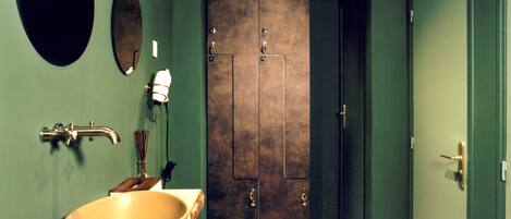 A bathroom with a large oval mirror, a round mirror, a sink with a bowl, a faucet, and a door with a handle.
