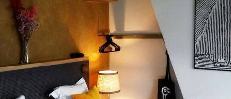 Una habitación de hotel con cama, almohadas, una lámpara, un jarrón con flores y un cuadro en la pared.