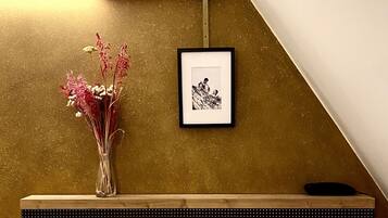 Una fotografía enmarco en la pared, un jarrón con flores en un estante y un escritorio de madera.