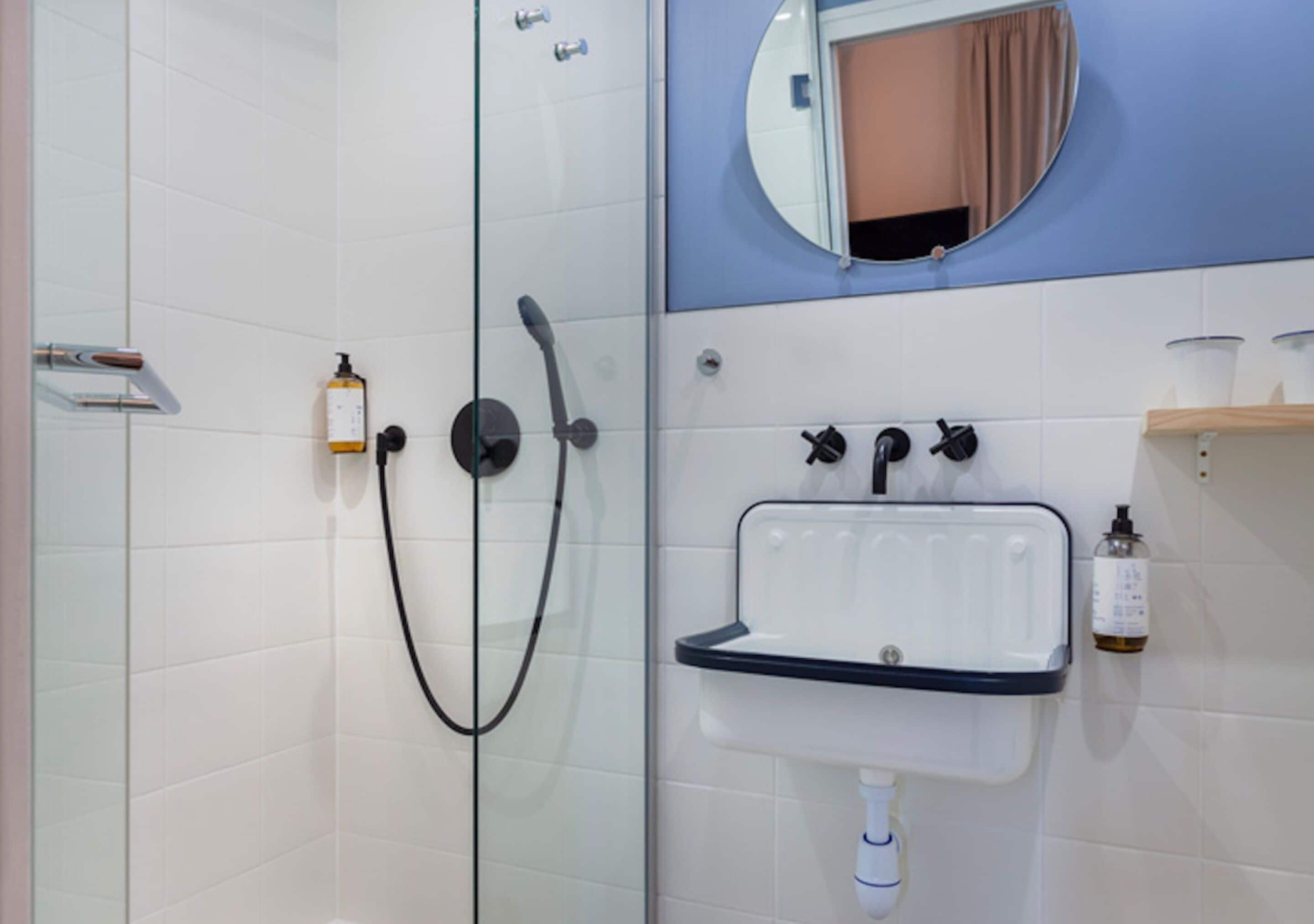 A bathroom with a glass shower enclosure, a sink with a mirror, and toiletries on the wall.