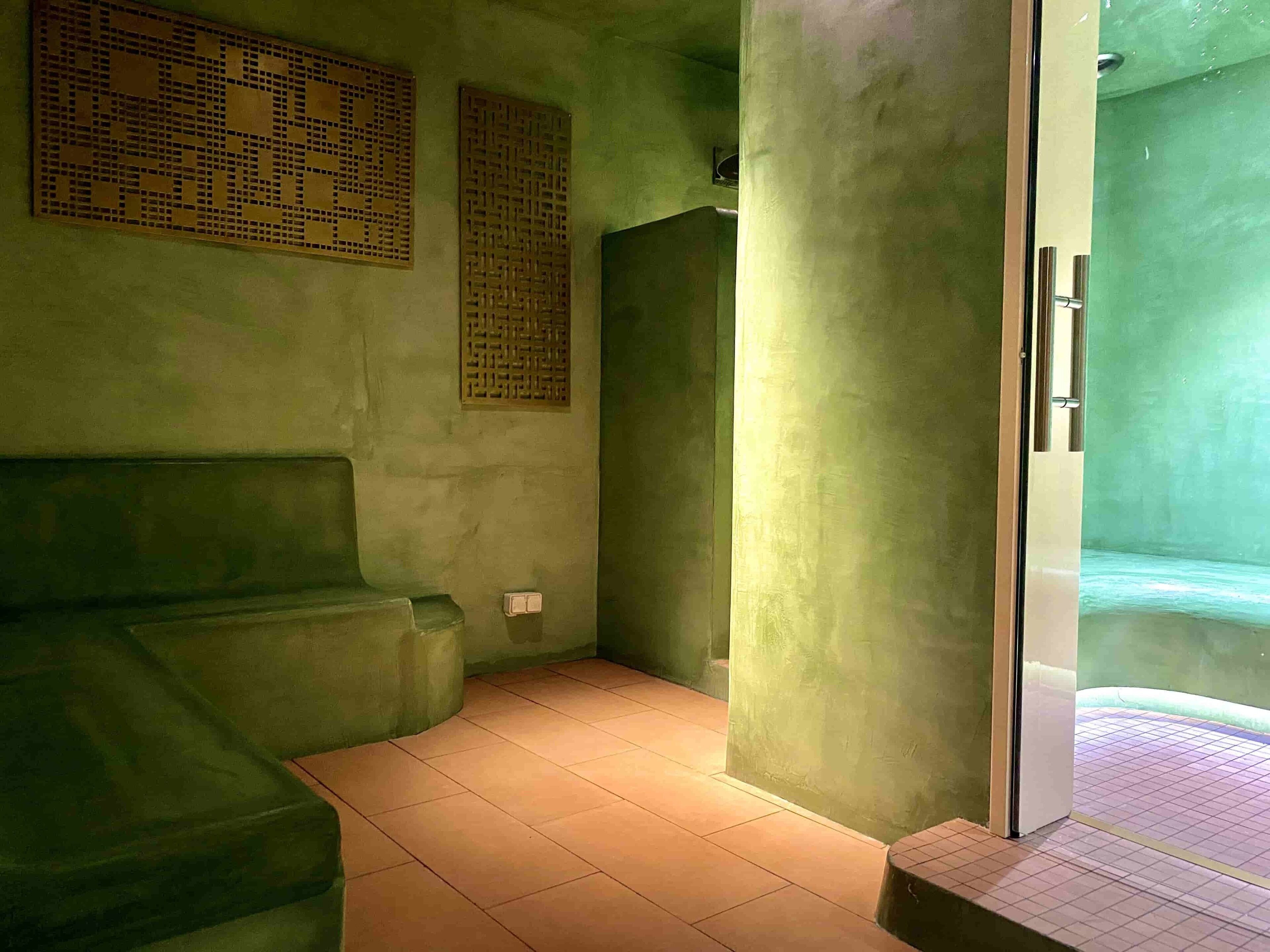 A room with a green wall, a bench, a door, and a tiled floor.