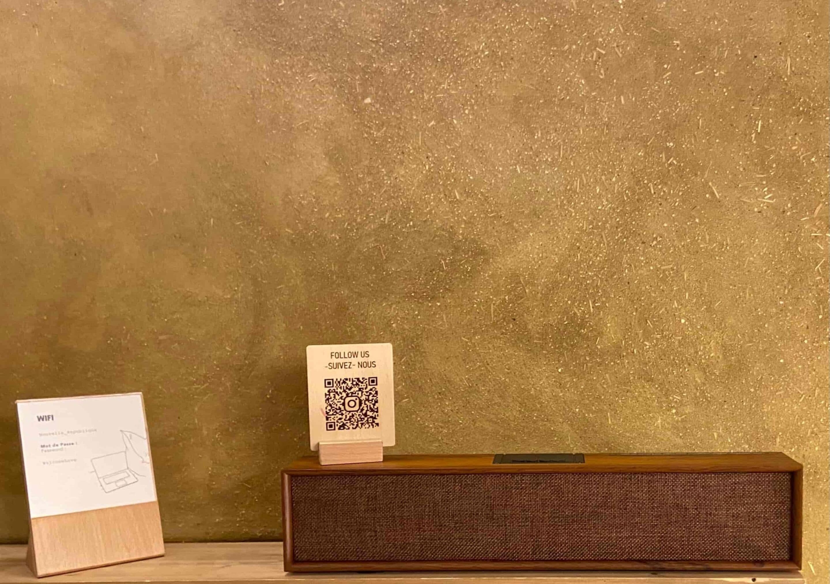 A wooden speaker and two informational signs on a shelf against a textured wall.