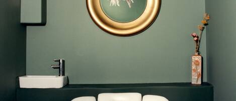 A bathroom with a white sink, a gold-framed mirror, and a vase with dried flowers on a dark counter.