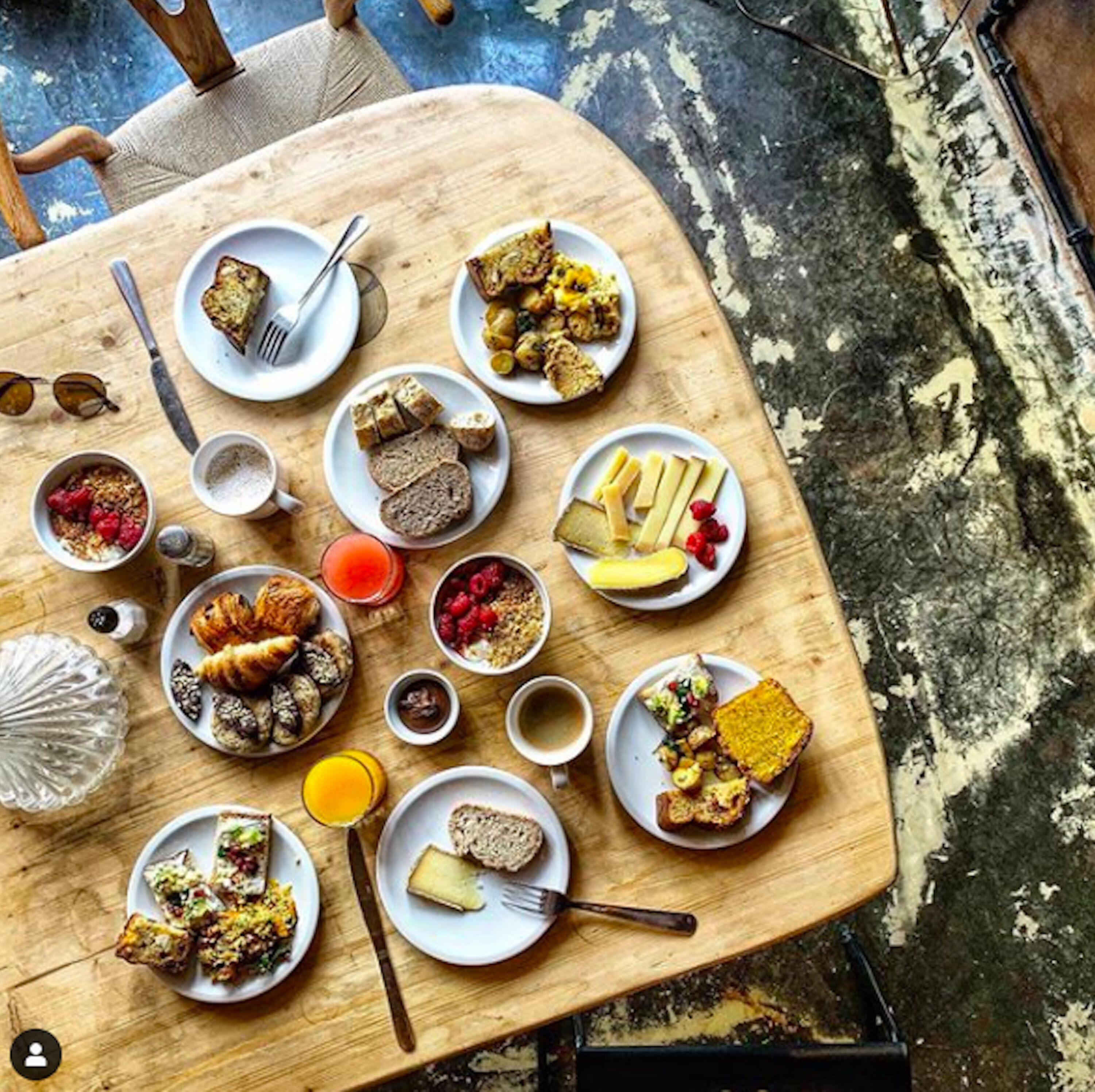 A breakfast spread on a wooden table with various dishes including toast, pastries, and fruits.