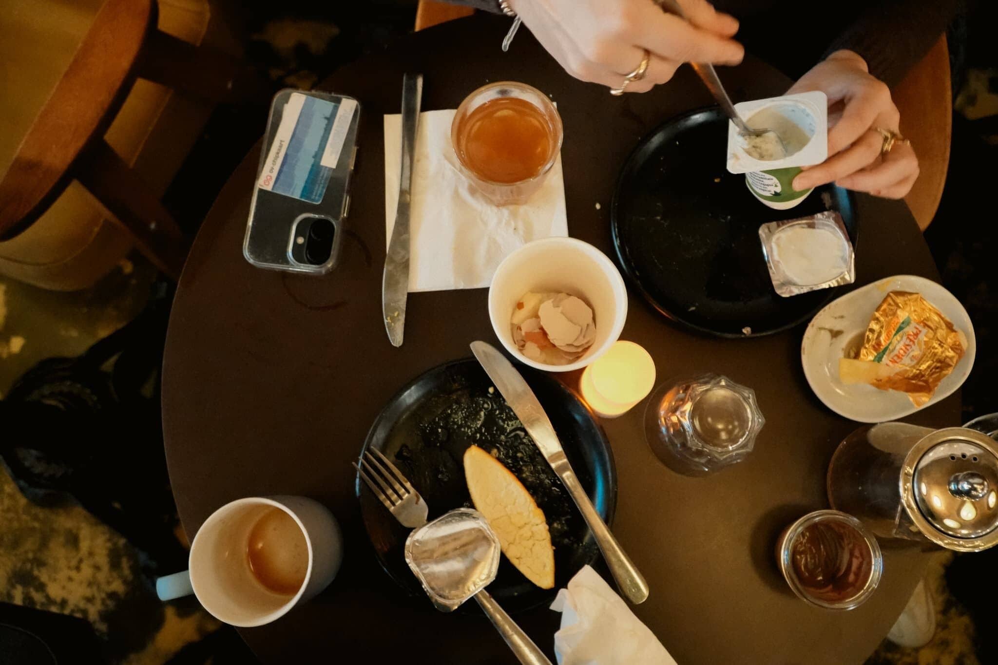 Een eettafel met verschillende soorten eten, bestek en een smartphone.