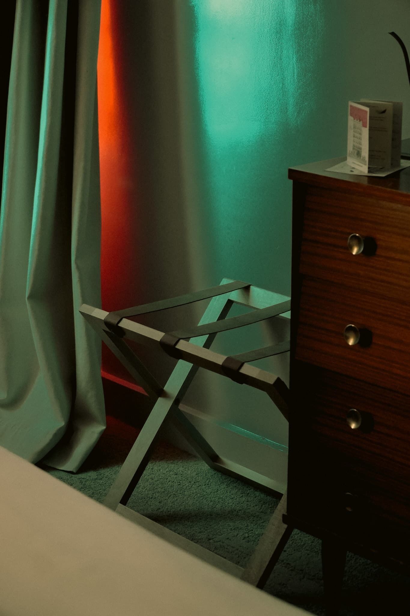 Una habitación con escritorio, silla, cómoda de madera y cortina.
