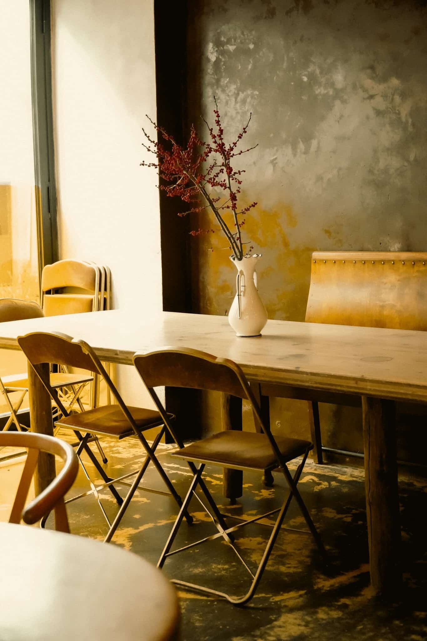 Un comedor con una mesa, sillas y un florero con ramas.