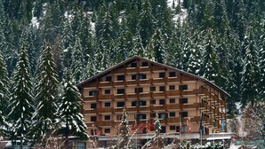 A multi-story lodge with a wooden facade, surrounded by snow-covered trees and a stone wall. - Hotel Il Caminetto (Canazei)