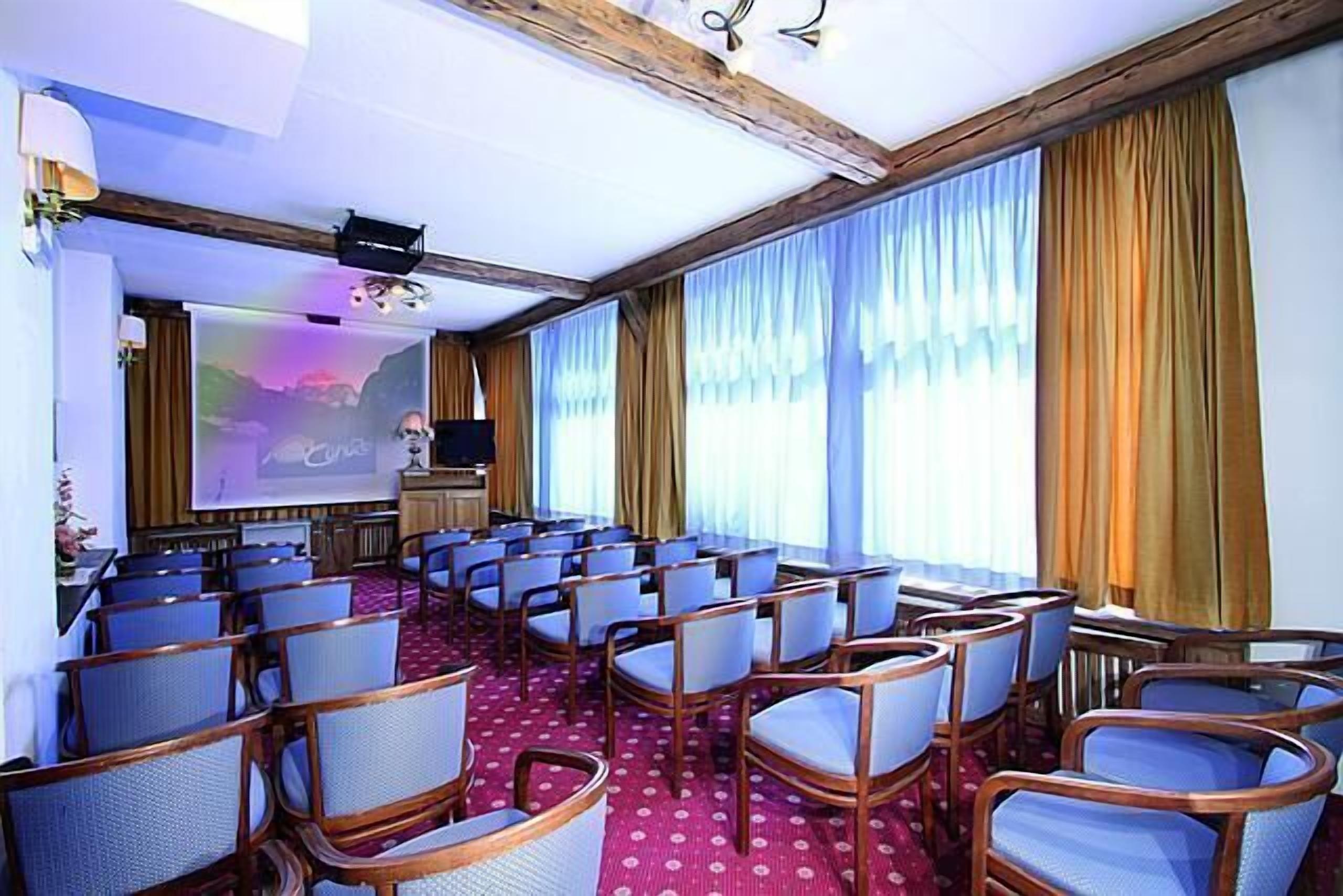 A conference room with rows of chairs, a projector screen, and a large window with curtains.