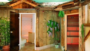 A wooden interior with a bathroom, a potted plant, and a door with a red light. - Hotel Il Caminetto (Canazei)