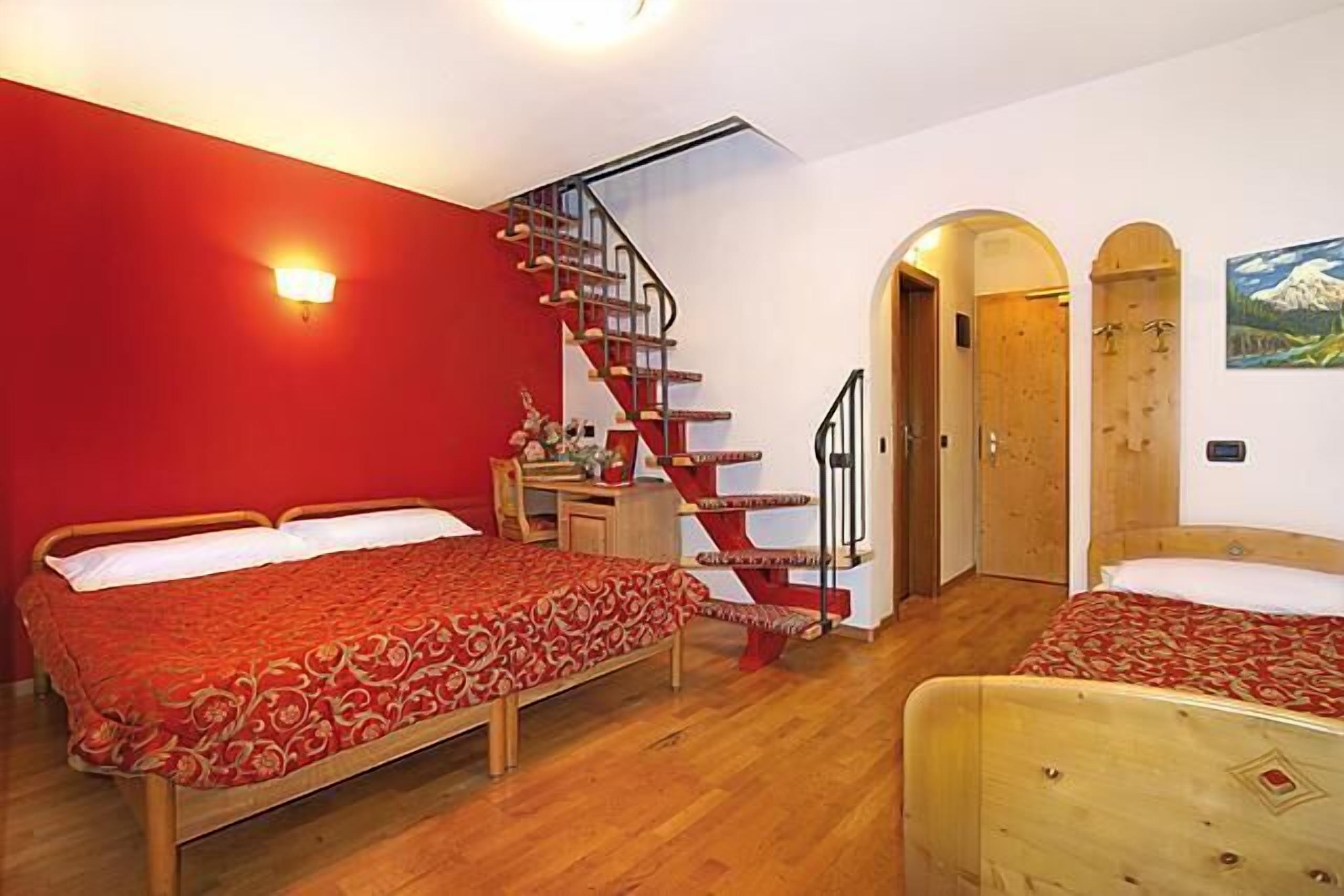 A room with two beds, a wooden staircase, a desk, and a door.