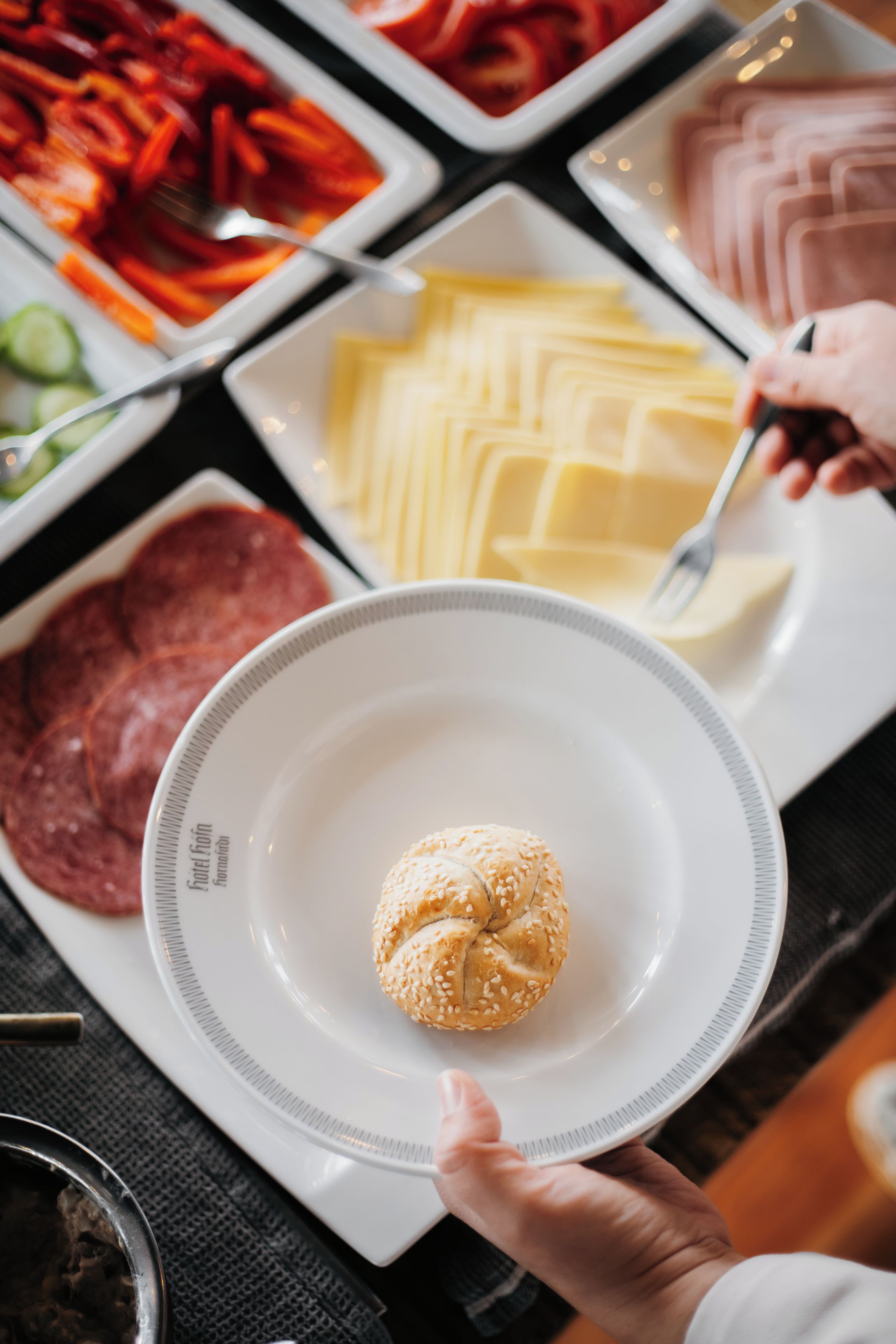 Una mesa de buffet con diversos alimentos, incluyendo carnes en lonchas, verduras y un plato con un pan de sésamo.