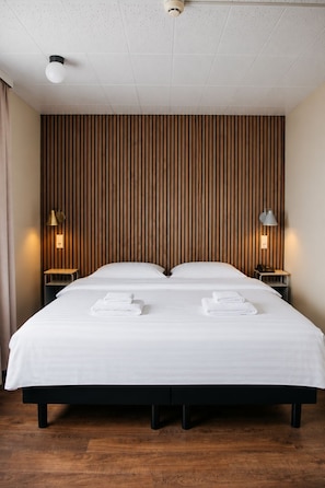 A double bed with white linens and two towels, a wooden slat wall, two bedside lamps, and a ceiling light. - Hotel Höfn (Höfn)