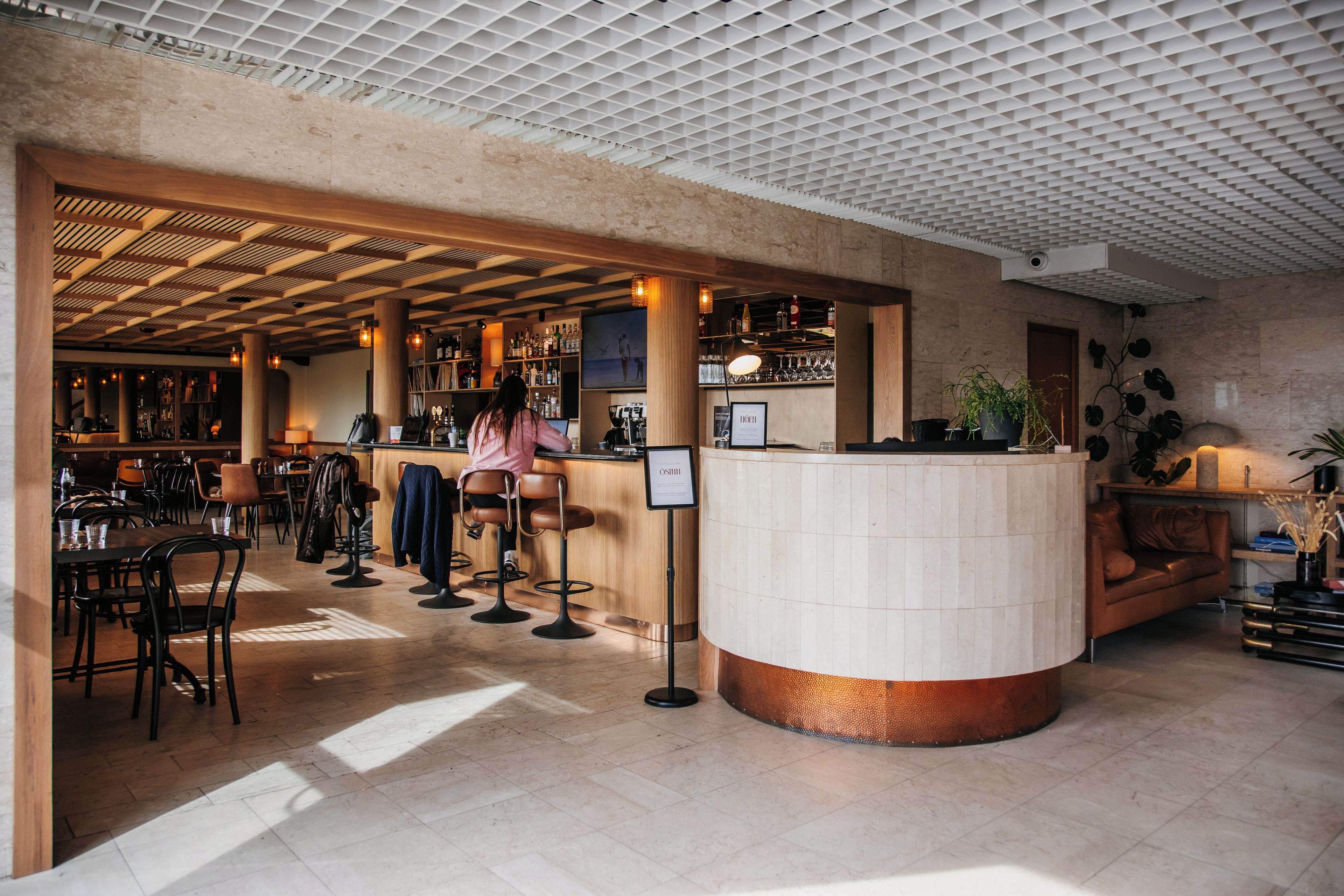 Zona de bar con barra, taburetes y área de estar con mesas y sillas.