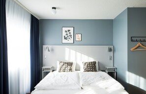 A modern hotel room with a large bed, bedside tables, a wall-mounted light fixture, and a coat rack. - Hotel Höfn (Höfn)