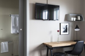 A modern hotel room with a wooden desk, a black chair, a flat-screen TV mounted on the wall, a framed picture, a vase with a rose, a coffee machine, and a shelf with cups. - Hotel Höfn (Höfn)