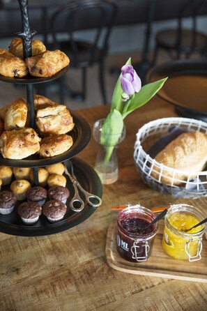 A three-tiered stand with pastries, a basket with a loaf of bread, and jars of jam on a wooden table. - Hotel Höfn (Höfn)