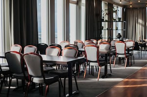 Un'area pranzo moderna con diversi tavoli e sedie, ampie finestre e vista sulla città.