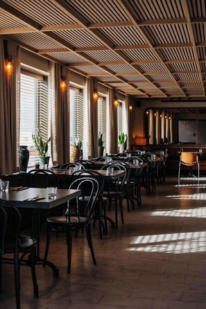 A restaurant with multiple tables and chairs, a wooden ceiling, and large windows with curtains. - Hotel Höfn (Höfn)