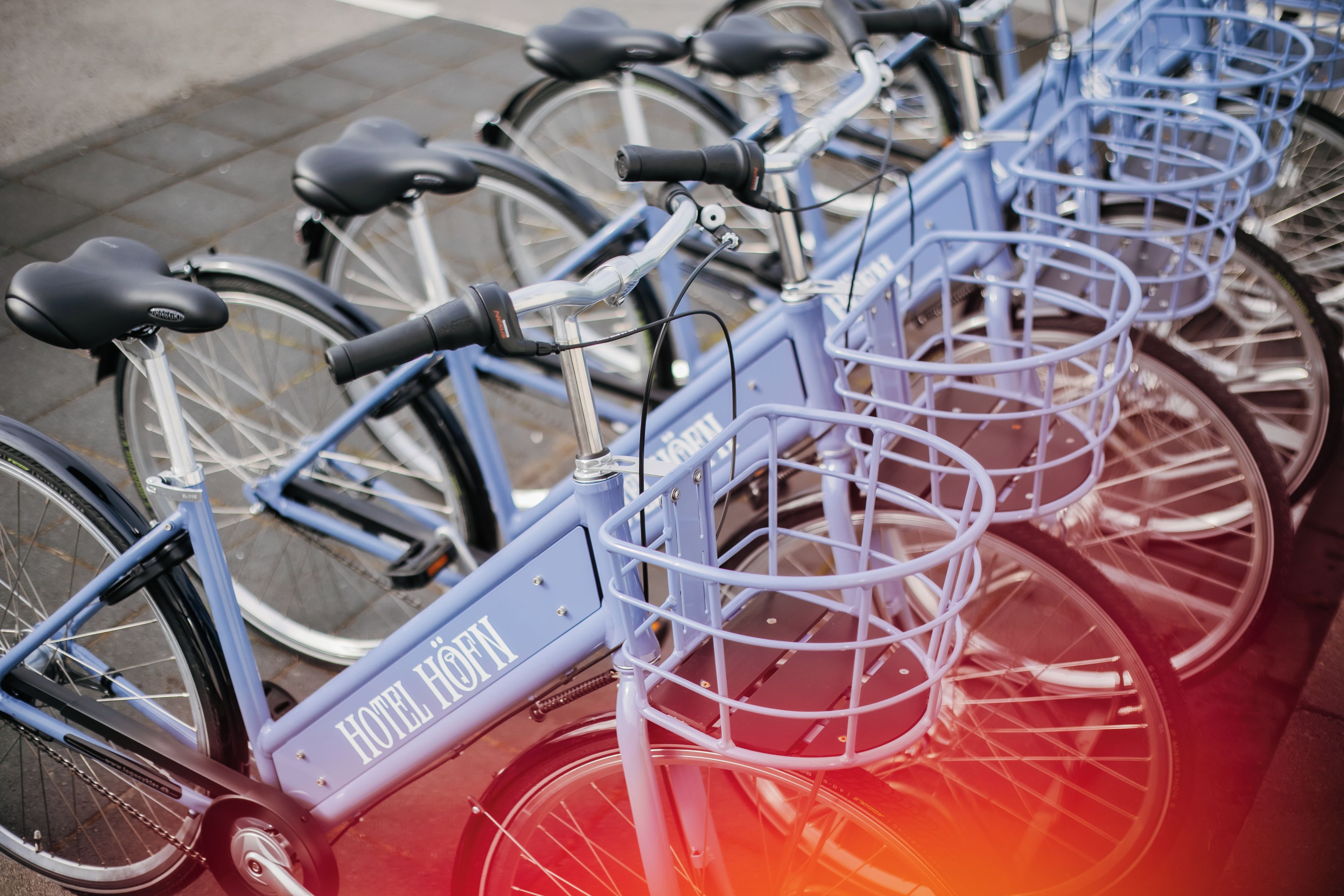 A row of bicycles with baskets, labeled 'HOTEL HOFEN,' parked on a sidewalk.