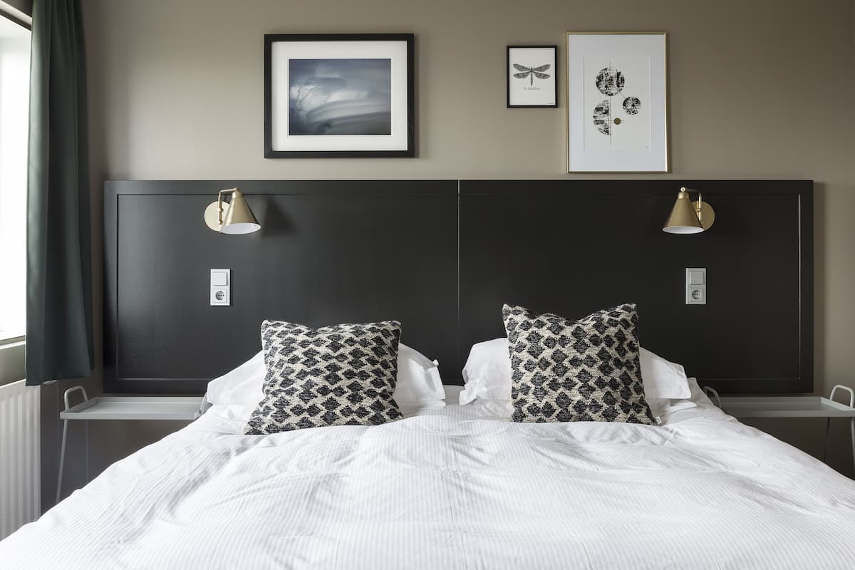 A neatly made bed with patterned pillows, a dark headboard, and two wall-mounted lamps.