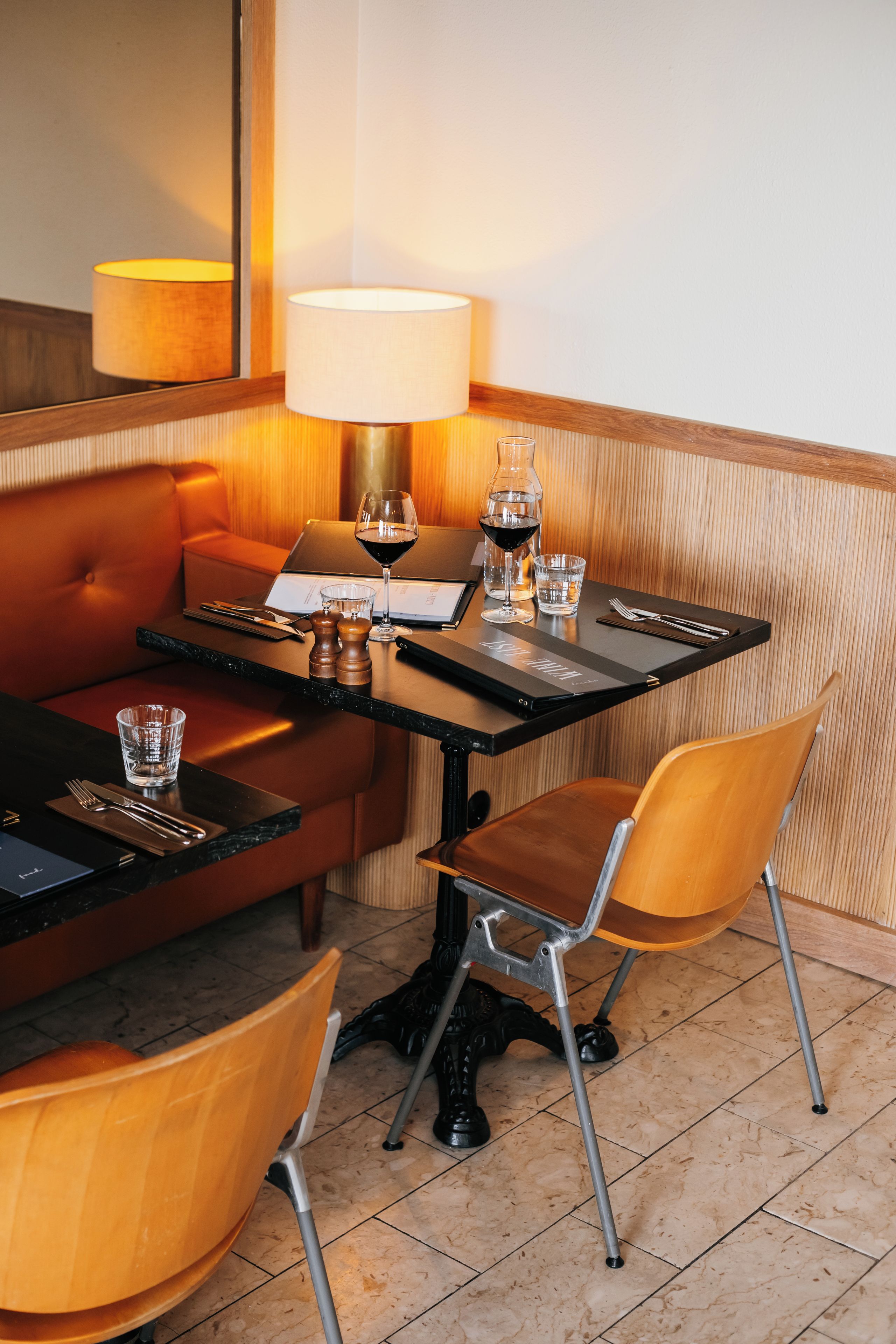 A hotel room with a dining table, two chairs, a sofa, a lamp, a wine glass, and a bottle.