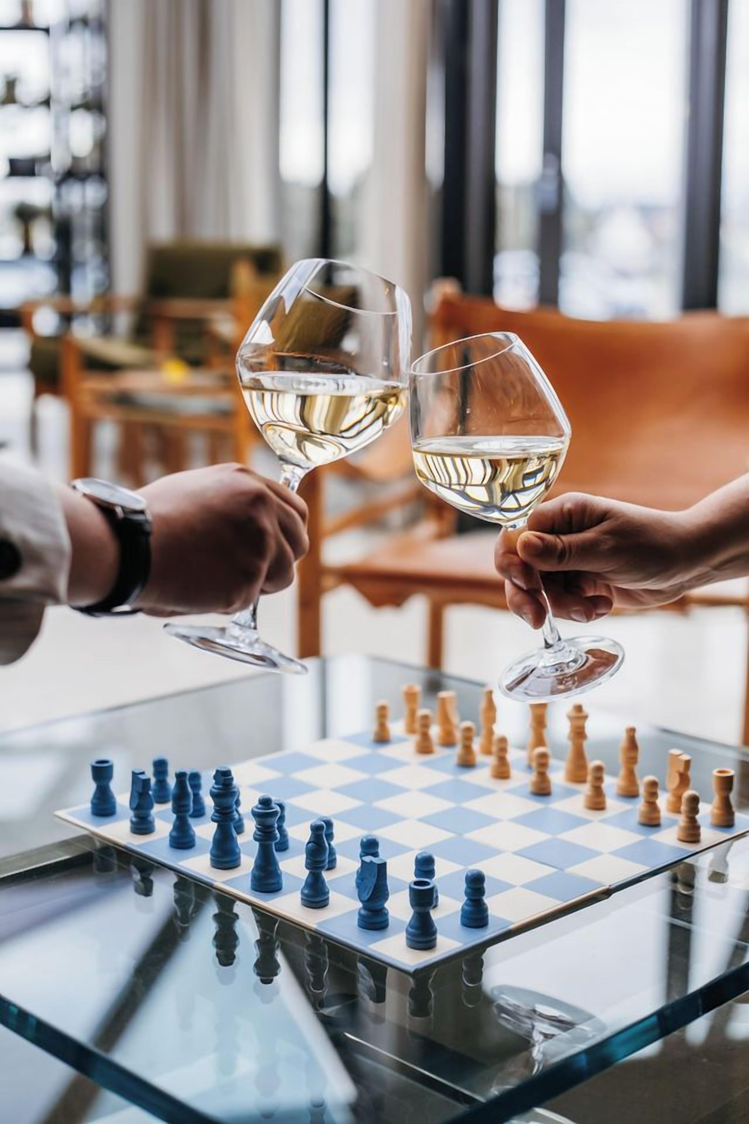 A chessboard on a glass table with two glasses of white wine.