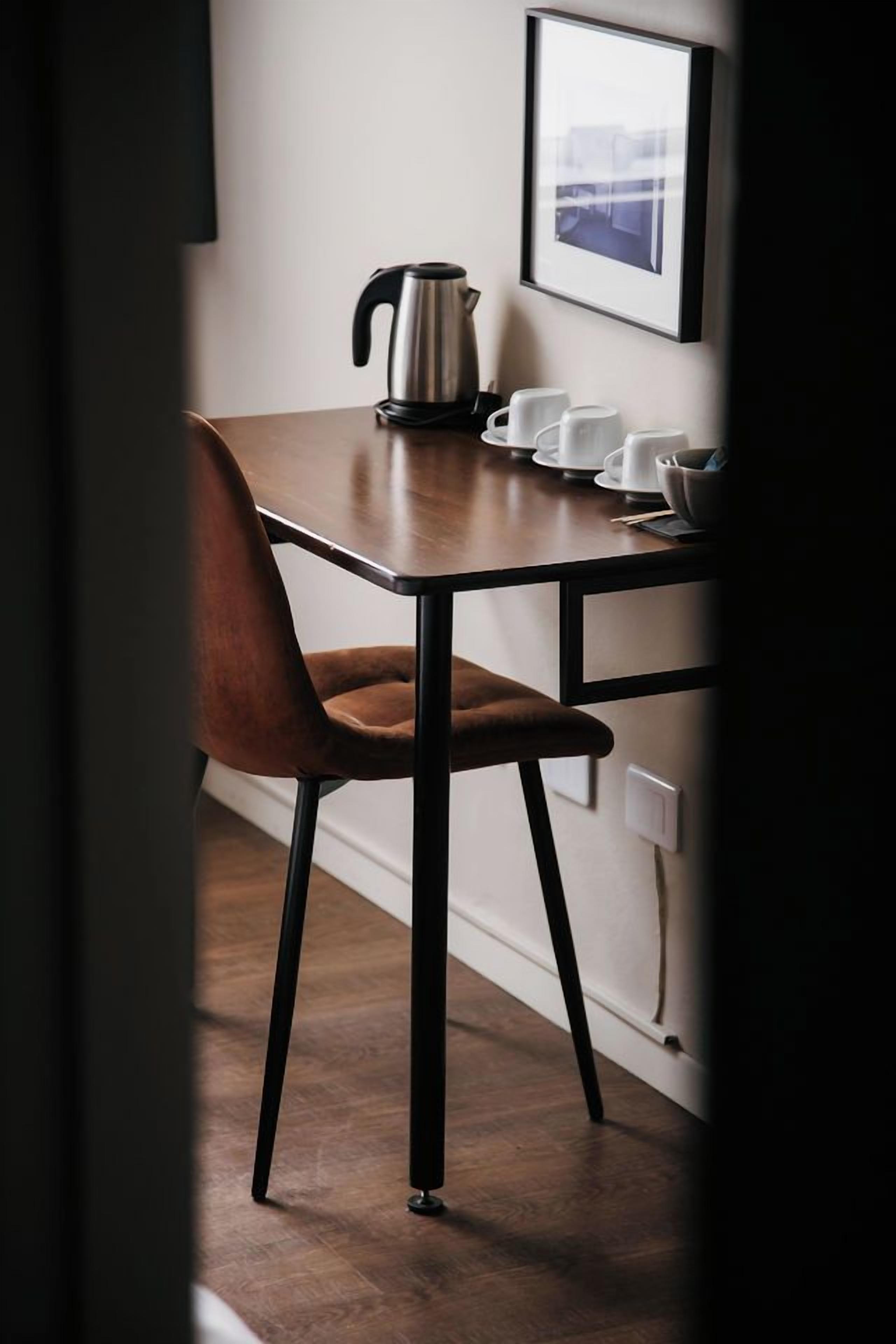 A dining area with a table, chairs, a kettle, and a framed picture on the wall.