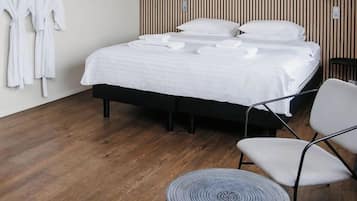 Una habitación de hotel moderna con una cama grande, dos mesitas de noche, una silla y un perchero en la pared.
