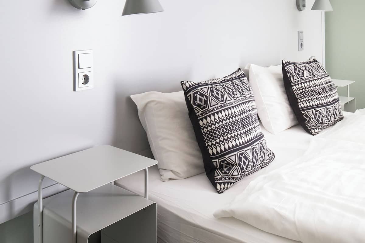 A hotel room with a bed, bedside tables, a desk, and wall-mounted lamps.