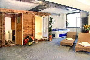 A spa room with wooden walls, a hot tub, two wicker chairs, and potted plants. - Hotel Grohmann (Campitello di Fassa)
