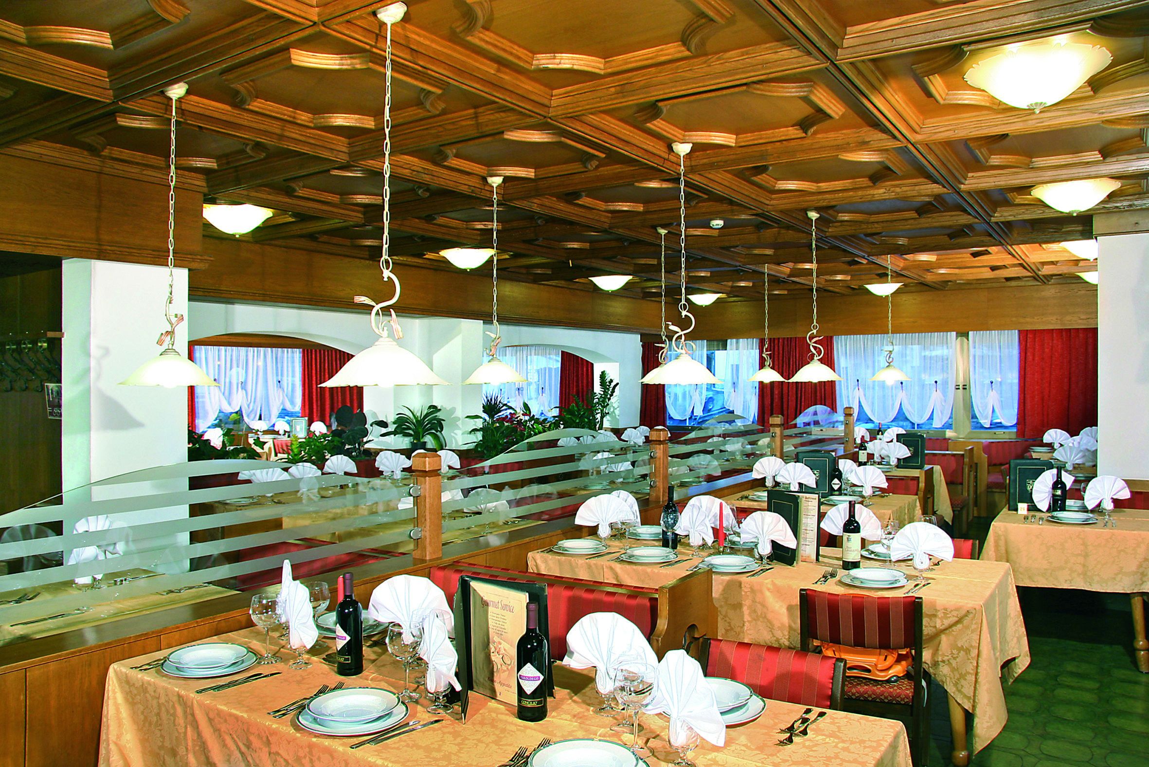 Ein Restaurant mit mehreren gedeckten Tischen, das durch hängende Leuchten und eine Holzbalkendecke gekennzeichnet ist.