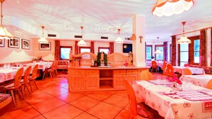 A restaurant with multiple tables and chairs, a central island, and hanging lights. - Albergo Villetta Maria (Canazei)