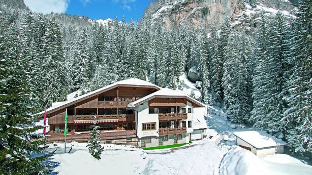 A multi-story lodge with a wooden exterior, surrounded by snow-covered trees and mountains. - Albergo Villetta Maria (Canazei)
