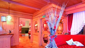 A hotel lobby with a red sofa, a decorative plant, and a wooden reception desk. - Albergo Villetta Maria (Canazei)