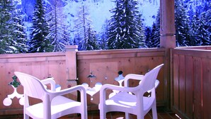 A wooden deck with two white plastic chairs and a small table, overlooking a snowy mountain landscape. - Albergo Villetta Maria (Canazei)