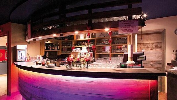 A bar area with a curved counter, shelves with bottles, and a sign above. - Bellevue Hotel (Canazei)