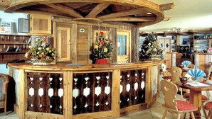 A rustic wooden bar area with a curved ceiling, surrounded by wooden chairs and tables. - Bellevue Hotel (Canazei)
