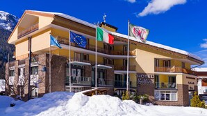 A hotel with multiple balconies, flags, and a snow-covered roof. - Bellevue Hotel (Canazei)