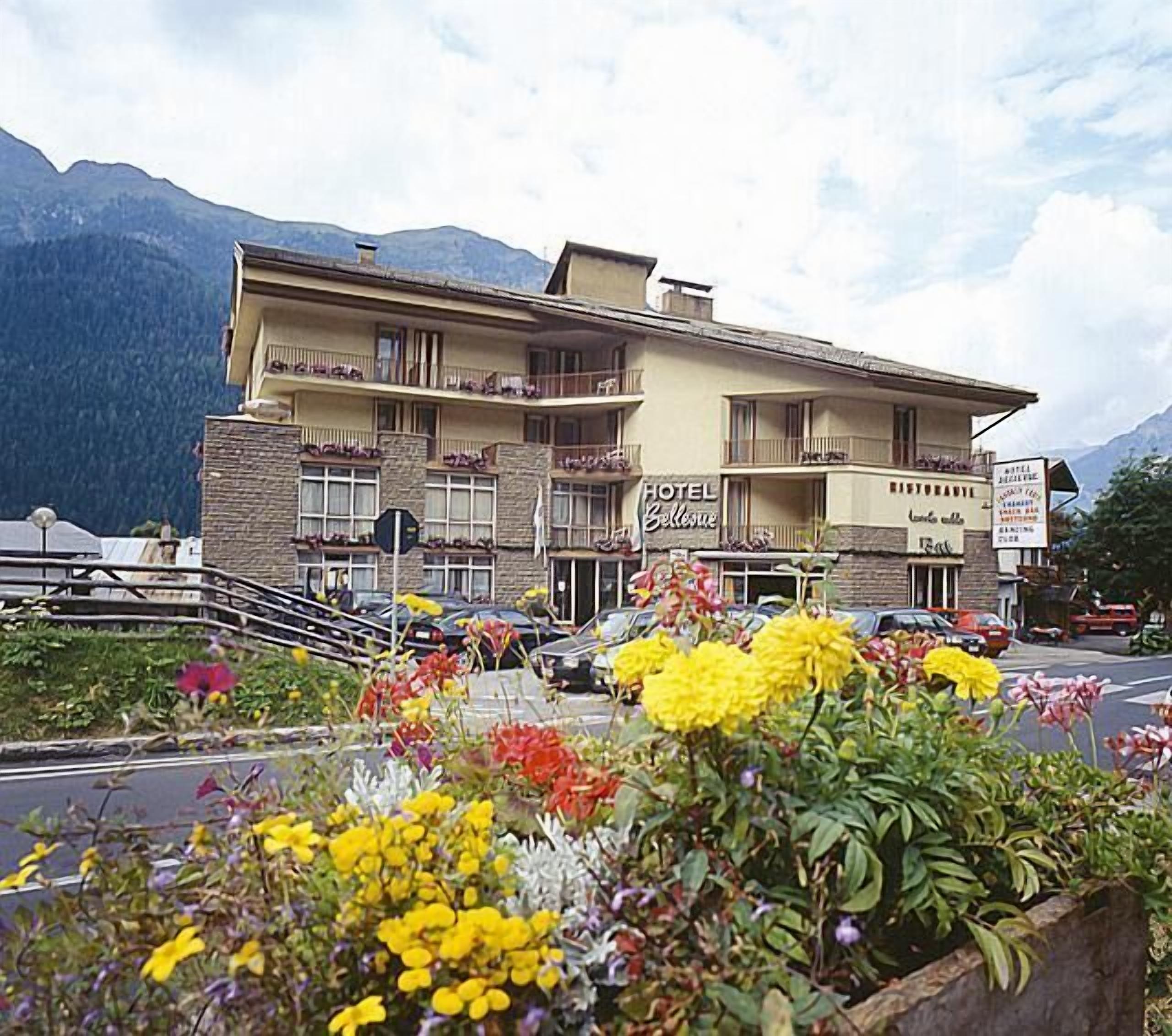 A hotel with a balcony, a sign reading "HOTEL Bellevue," and a mountain backdrop.