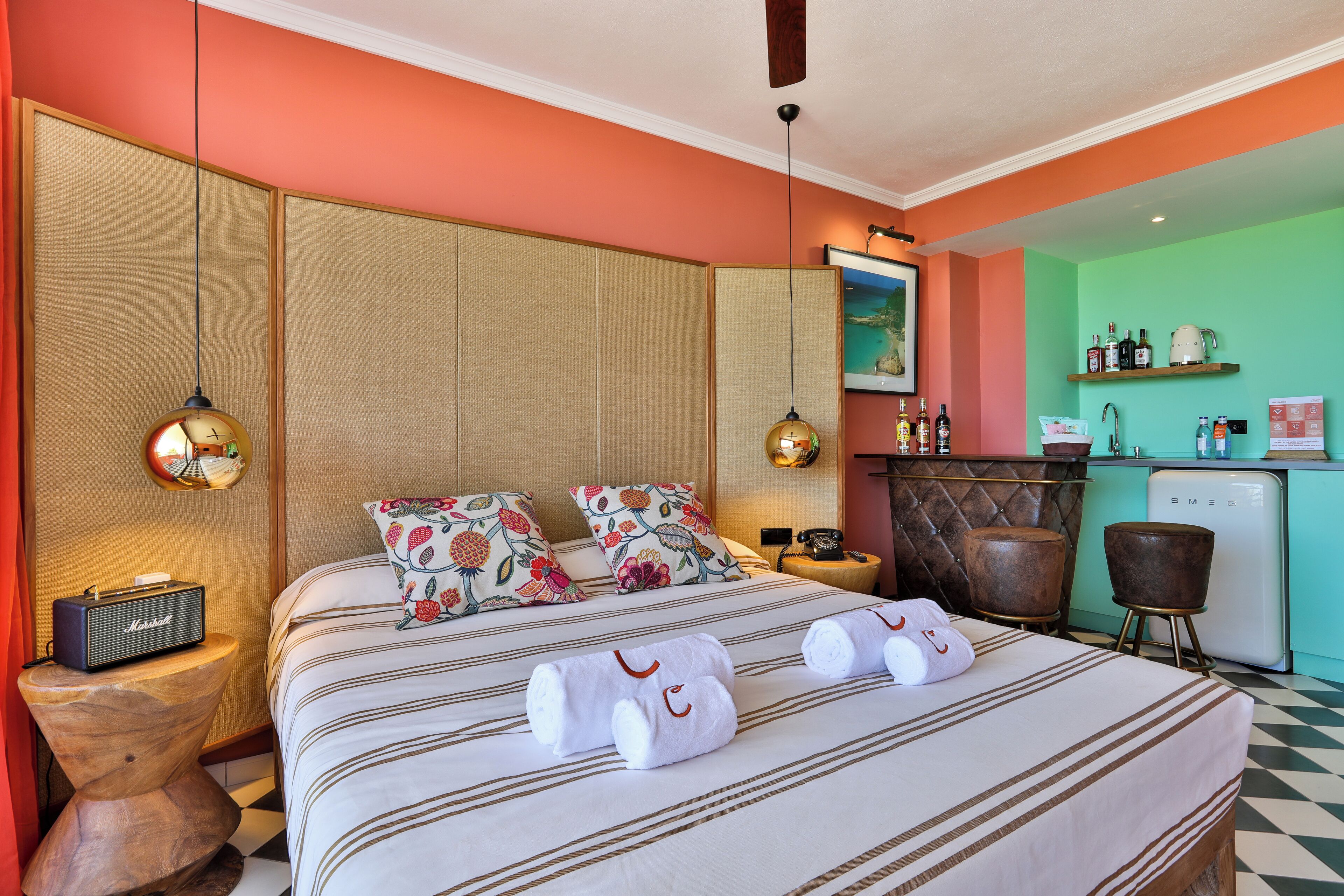 Una habitación de hotel con cama, mesitas de noche, minibar y kitchenette.