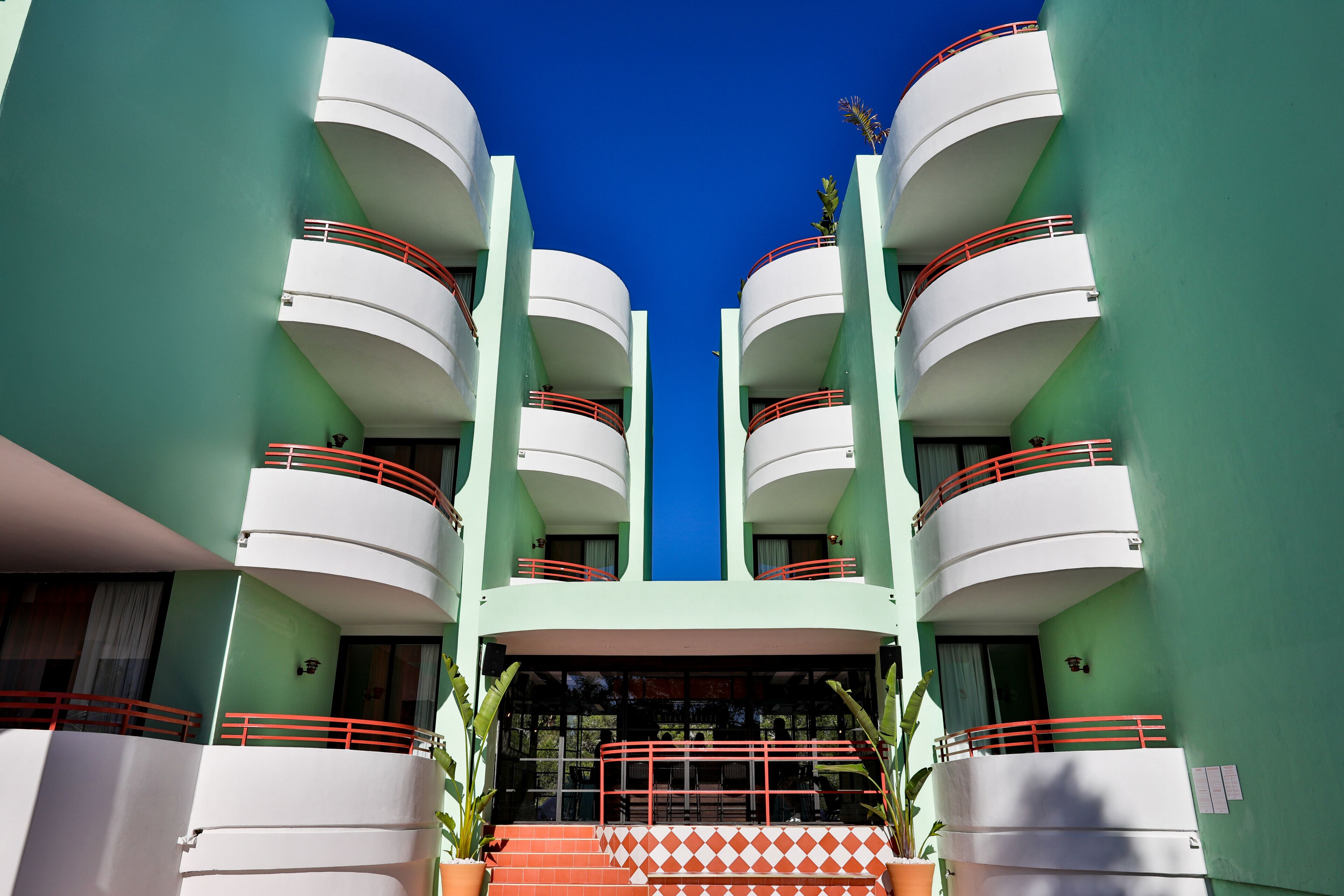 A modern hotel with a symmetrical facade, multiple balconies, and a central entrance with steps.