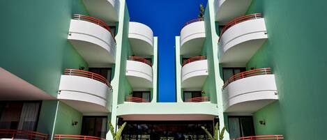 A modern hotel with a symmetrical facade, multiple balconies, and a central entrance with steps.
