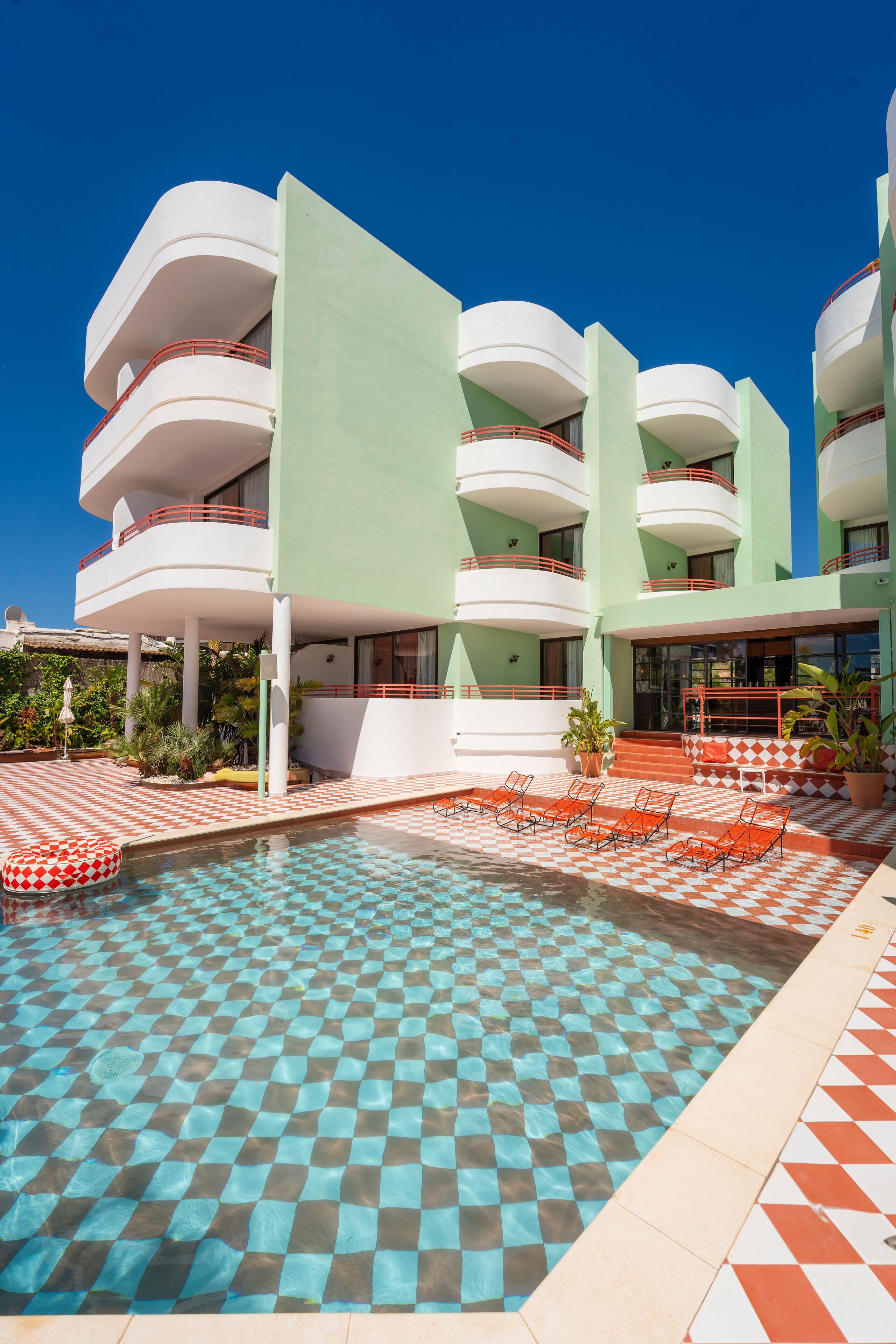 A hotel with a pool area featuring checkered tiles, outdoor seating, and a modern architectural design.
