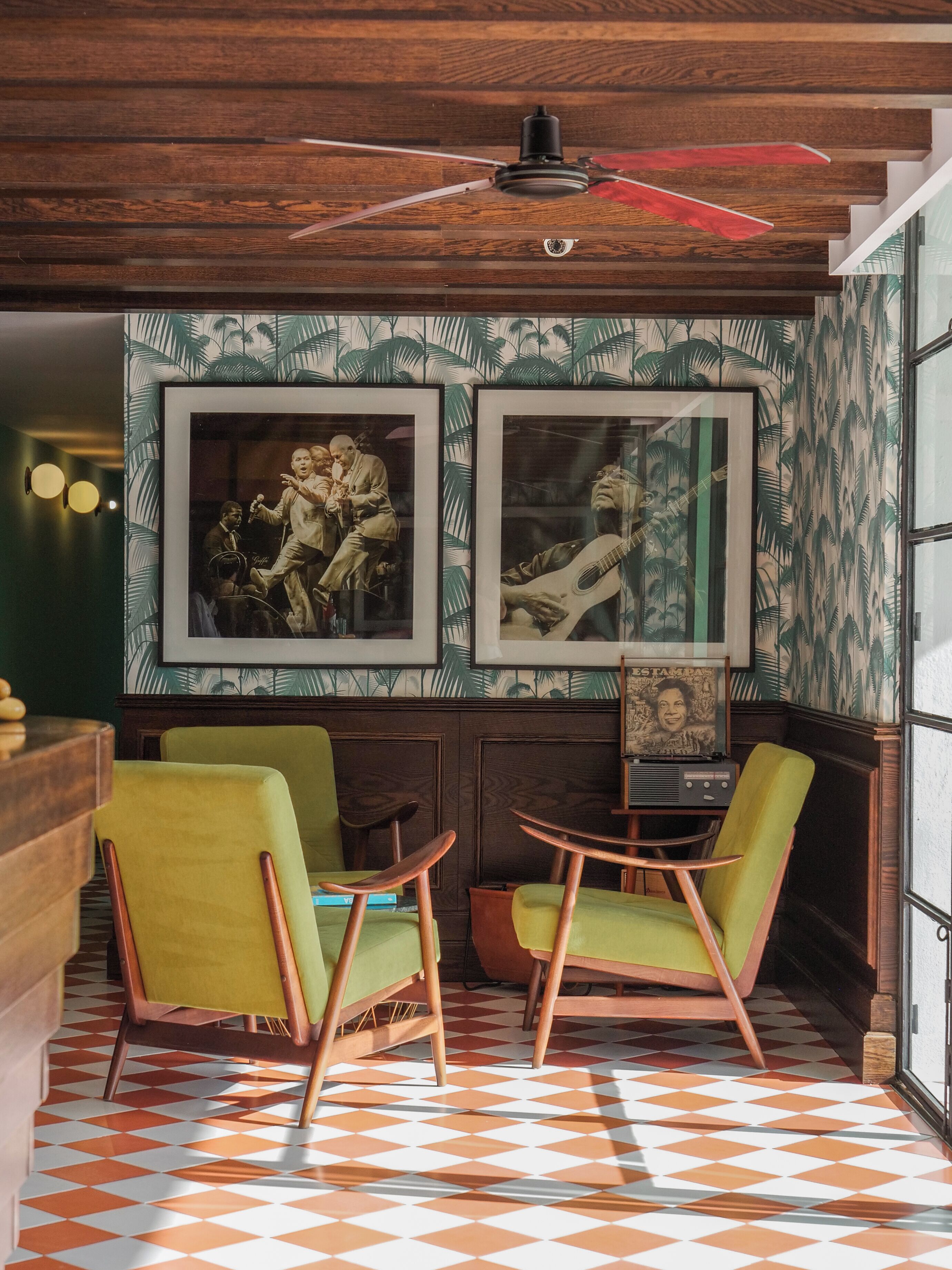 Una habitación con dos sillones verdes, techo de madera y papel tapiz estampado.