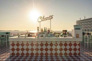 Uma área de bar com um letreiro 'Cubanito', piso xadrez e vista para o mar.