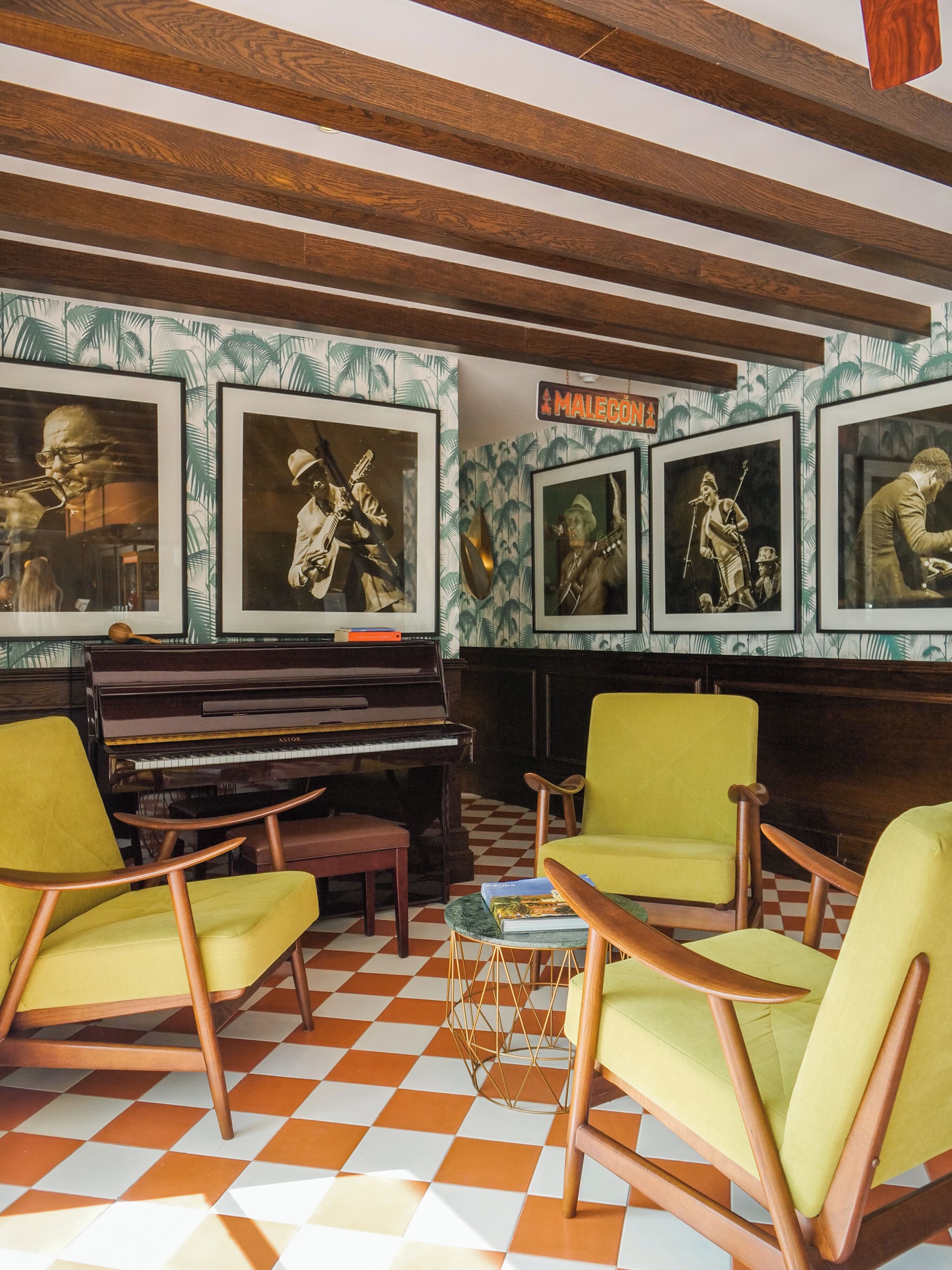A room with a checkered floor, a grand piano, and green armchairs.