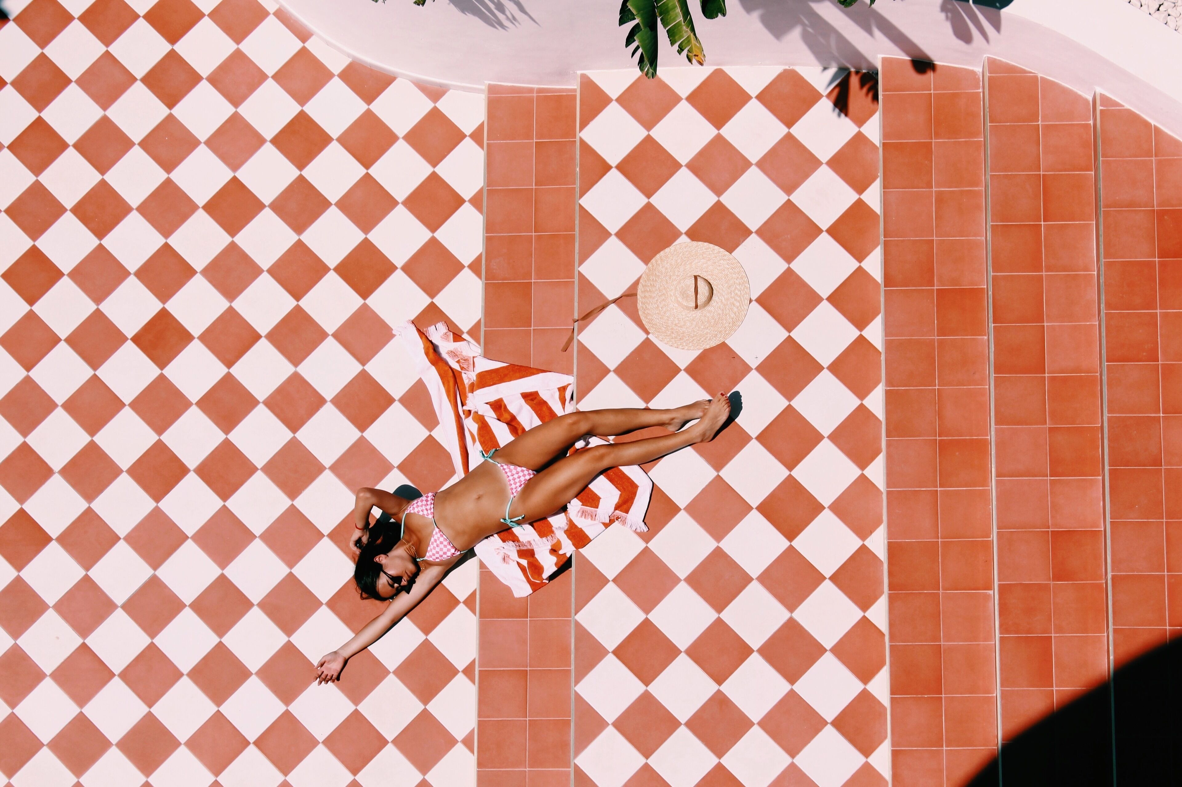 A person lying on a checkered floor with a towel and a hat.