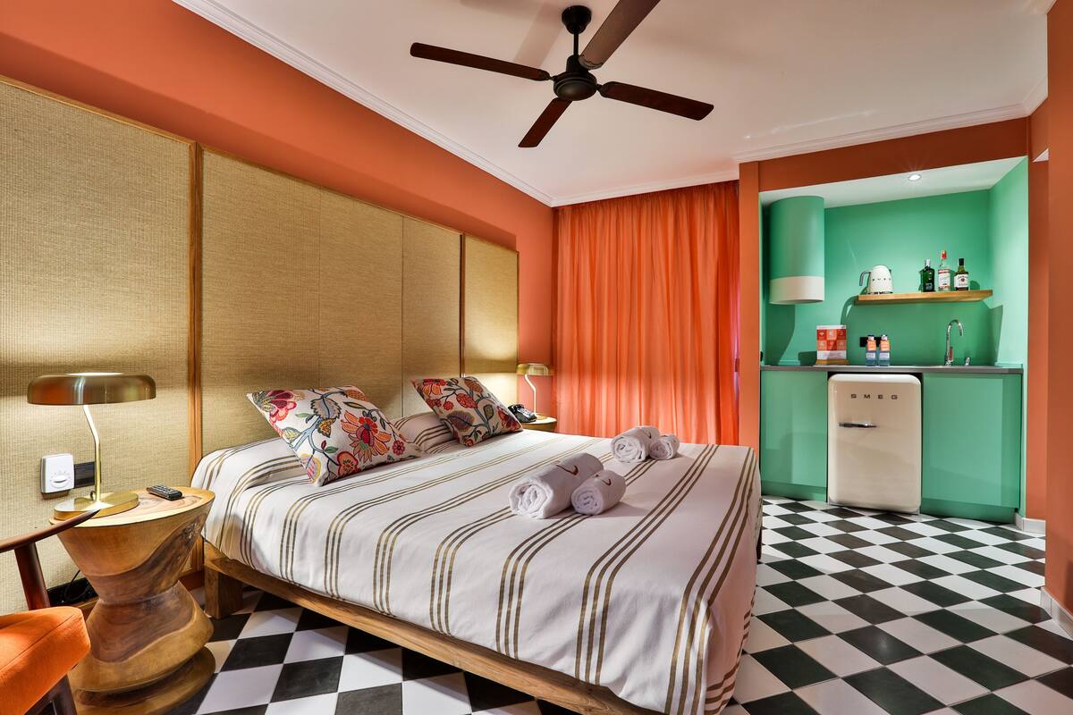 Une chambre d’hôtel équipée d’un lit, d’un bureau, d’une chaise, d’un ventilateur de plafond, d’un mini-bar et d’un comptoir d’enregistrement.
