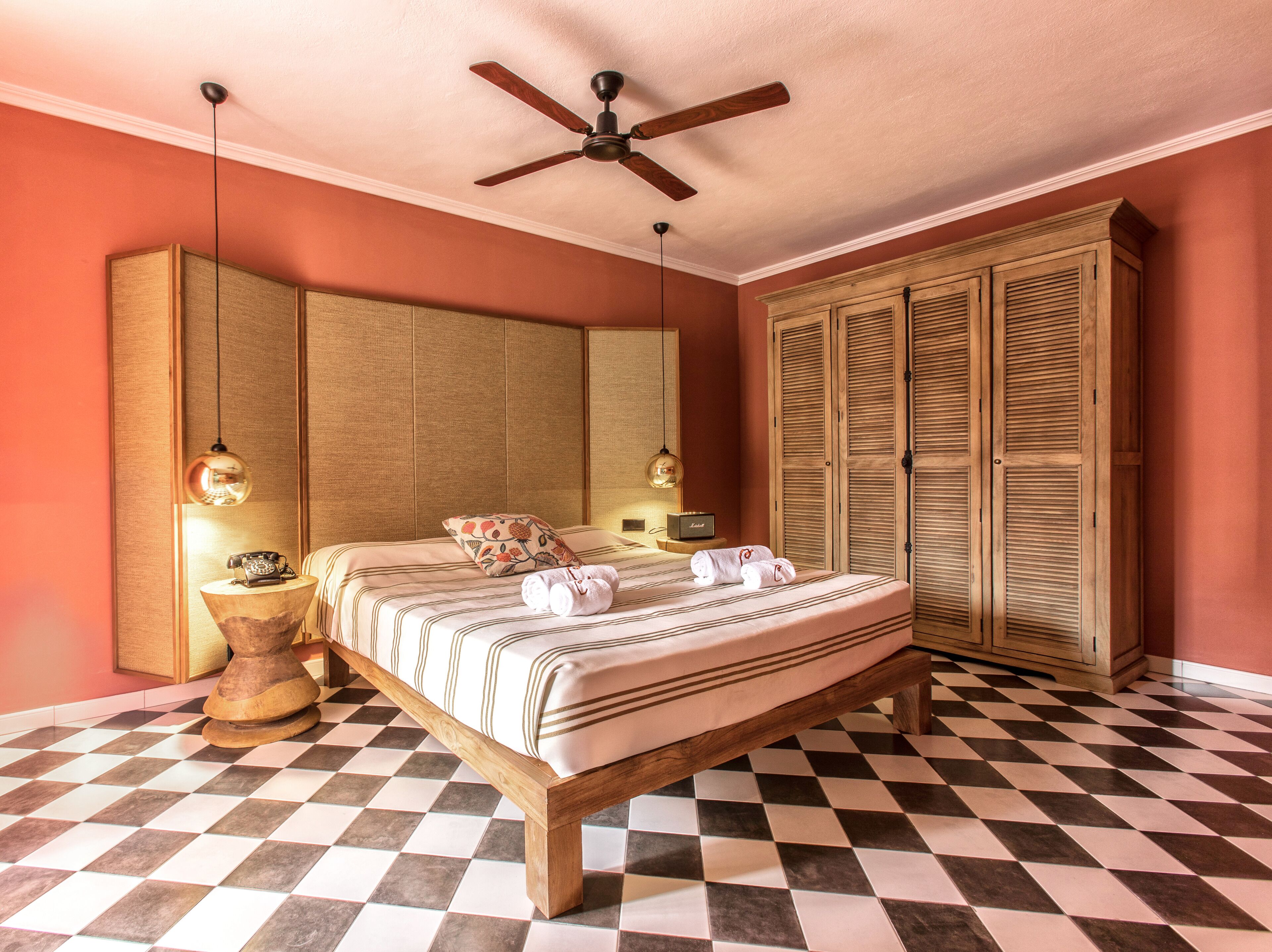 Una habitación con piso a cuadros, cama con ropa de cama a rayas, ventilador de techo y armarios de madera.